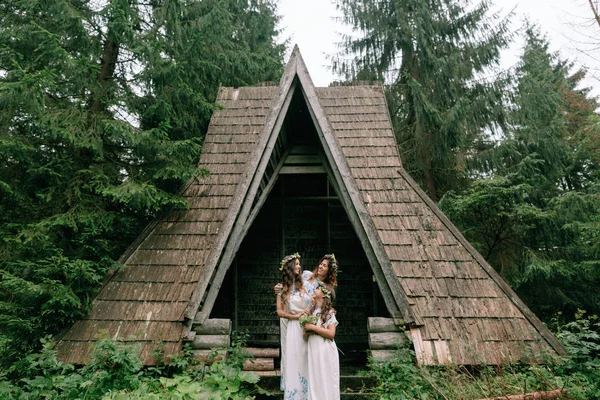 Anne ve iki kızı beyaz elbiseler kır çiçekleri çelenk ile göle yakın yürüyüş