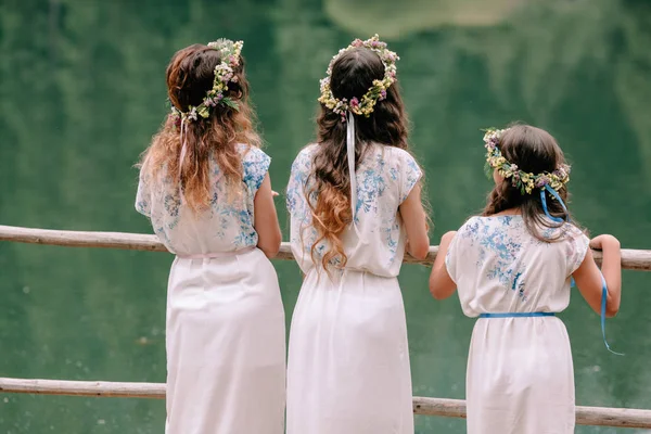 Anne ve iki kızı beyaz elbiseler kır çiçekleri çelenk ile göle yakın yürüyüş