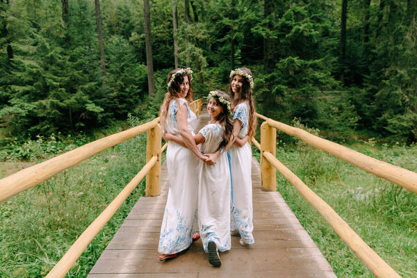 Mom and two daughters walking near the lake in white dresses with wreaths of wildflowers