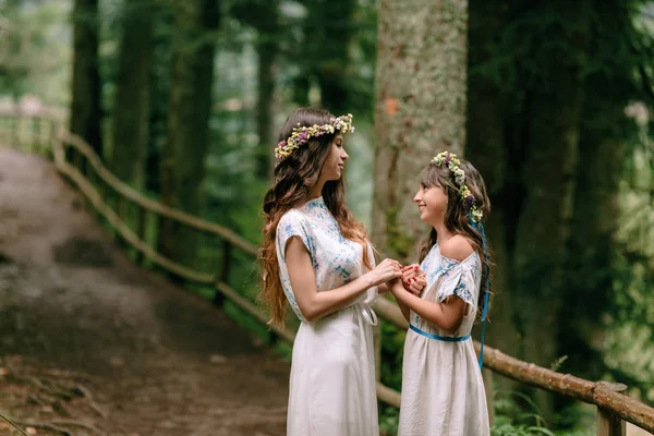 Mom and two daughters walking near the lake in white dresses with wreaths of wildflowers