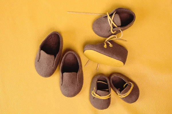 Brown, children's handmade shoes made of merino wool on a bright yellow background.