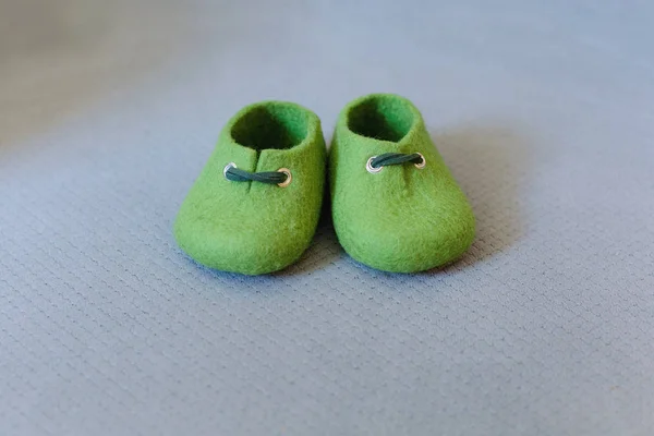 Green children's handmade shoes made of merino wool on a gray background.