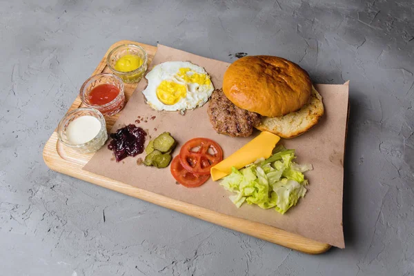 Gri beton zemin üzerine ahşap bir gemide bir burger için malzemeler.