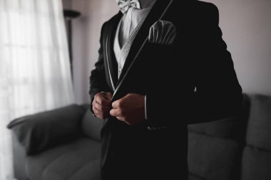 Siyah smokinli ve gri papyonlu damat ceketinin düğmelerini doğru takıyor. Adam ceketini giyer. Düğün detayları. Düğün hazırlıkları..
