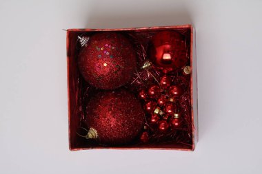Kırmızı Noel süslemeleri beyaz arka planda kare bir kutuda. Üç top, boncuklar.