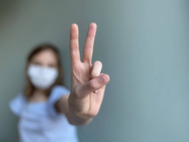 Victory sign shown by girl wearing surgical mask  clipart