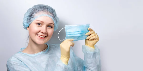 En ung, stilig läkare i medicinsk uniform tar på sig en medicinsk mask.. — Stockfoto