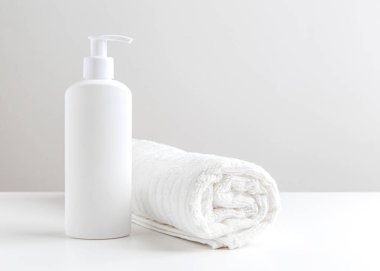 Beyaz bir havlu ve beyaz bir masada bir şişe kişisel bakım ürünü. Ön manzara. Tek renkli, beyaz renk. Minimalist tasarım.