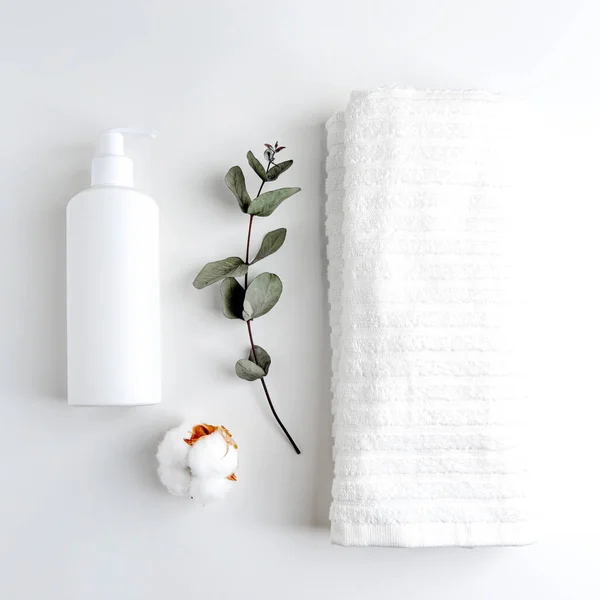 A white towel and a bottle of self-care products on a white table. Front view. Monochrome white color. The minimalist design.