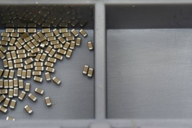 Abstract close-up of surface mount capacitor electronics components in storage container separated empty box
