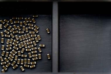 Abstract close-up of surface mount capacitor electronics components in storage container separated empty box