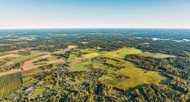Büyük orman, tarım alanları ve mavi bulutsuz gökyüzü arkaplanı ve ufukta hafif sis ile harmanlanmış yerleşim ve sanayi binaları ile kırsal köy üzerindeki sıcak hava eğrisi manzarası