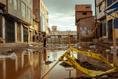 Desaguadero, Puno / Peru - 4 Nisan 2016: Büyük Kirli Su Çukuru ve Ürkütücü Tuğla Binaları olan Yırtık Ayrı Sokakta Kaykaylı Genç Adam