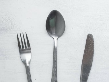 Bir demet çatal, kaşık ve bıçak kabaca boyanmış beyaz arka planda karıştırılmış.