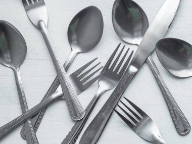 Bir demet çatal, kaşık ve bıçak kabaca boyanmış beyaz arka planda karıştırılmış.