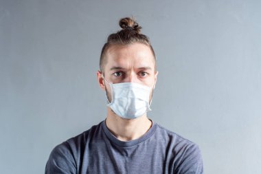 Genç, sarı saçlı, beyaz, tek kullanımlık yüz maskesi kullanan erkek. Cought, grip, virüs, viral koruma kameraya bakıyor.