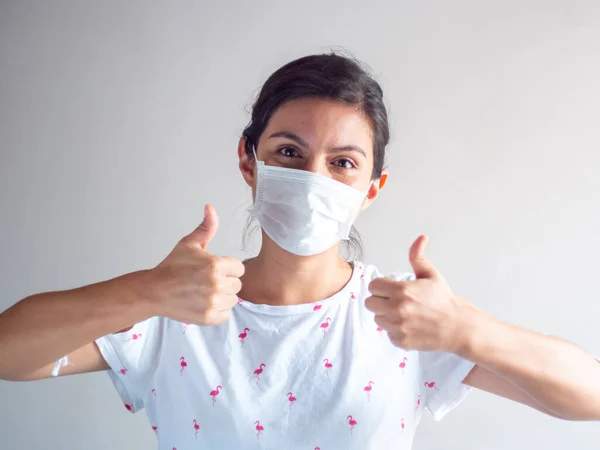 Young Attractive Brown Hair Hispanic/Latin Woman Using Disposable Face Mask for Cough, Flu, Virus, Viral Protection with Thumbs up