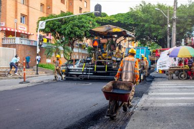 Medellin, Antioquia / Kolombiya - 19 Kasım 2019: Turuncu Üniformalı İnşaat İşçileri Bir Steamroller 'ın yanında bir el arabası kullanarak Sokakları Onarıyorlar
