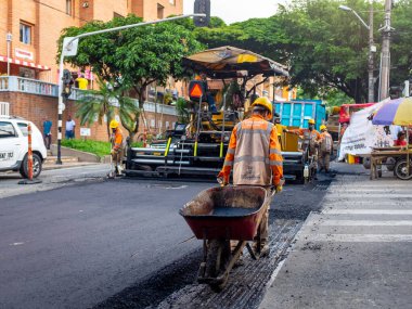 Medellin, Antioquia / Kolombiya - 19 Kasım 2019: Turuncu Üniformalı İnşaat İşçileri Bir Steamroller 'ın yanında bir el arabası kullanarak Sokakları Onarıyorlar
