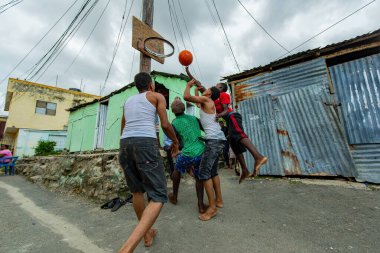 Santo Domingo / Dominican Republic - May 15 2018: Young Men Playing Basketball With a Car Rim in Poor Guandules Neighborhood clipart