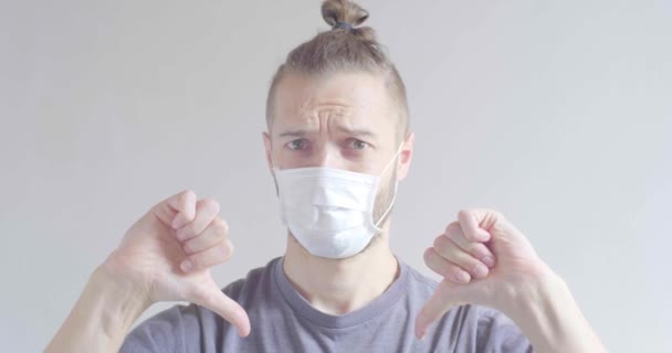 使い捨てフェイスマスクを使用した若いブロンドの髪白人男性Covid インフルエンザ ウイルス 親指ダウンでウイルス保護 — ストック動画