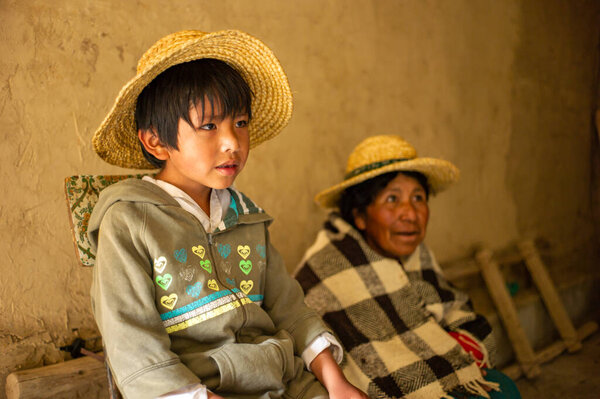 Poopo, Oruro / Bolivia - February 14 2018: Little Indigenous Uru Boy Wears a Straw Hat next to his Mother in his Home