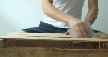 Beyaz bir arka planda ahşap bir kutu zımparalayan Genç Beyaz Adam Evde Kalır 