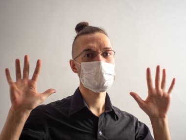 Siyah gömlekli ve gözlüklü genç sarı saçlı erkek Covid-19 için tek kullanımlık maske takıyor, yakalanmış, grip olmuş, virüs kapmış, viral koruma iki elini de gösteriyor.