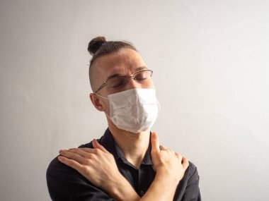 Siyah gömlekli ve gözlüklü genç sarı saçlı beyaz erkek Covid-19 için tek kullanımlık bir maske takıyor, yakalanmış, grip olmuş, virüsü kapmış ve kapalı gözlerle ona sarılıyor.