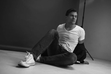 Stylish man posing in the studio on a black and white background. Dressed in a white shirt, blue jeans and sneakers