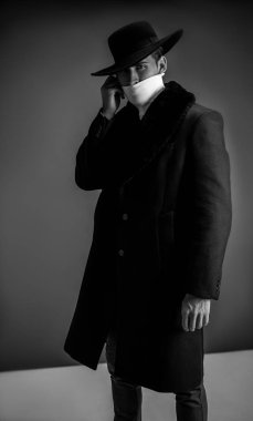 Fashion model posing on gray background in studio. Model tests. Man wearing in black coat, white golf and hat.