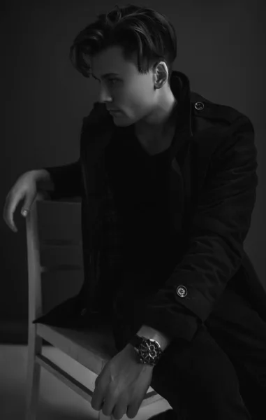 黒を基調とした椅子に座るファッションスタイリッシュな男 黒のコートを着て — ストック写真