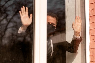 Karantina karantinası. İçeriden içeri bakan maskeli üzgün bir adam. Kendini izole eden tıbbi maskeli hasta bir adam.