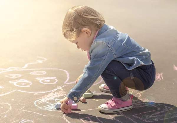Girl in a jeans jacket draws with colored chalks — Stock Photo, Image