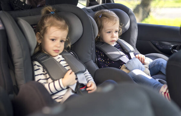 cute small twins in car seats in the car