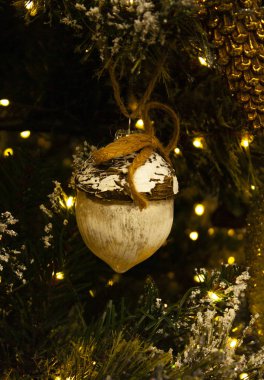 Noel süslemeleri meşe palamudu biçiminde ladin dallarında sallanırken arka planda ışık çelenklerine karşı