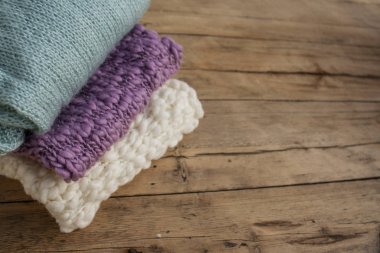 Üç farklı renkte örülmüş şeyler bir yığın halinde ahşap bir masanın üzerinde duruyor..