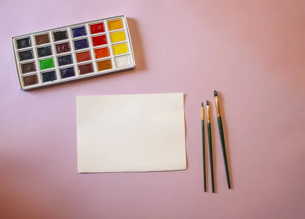 ピンクの背景に白い紙と水彩絵具と筆で — ストック写真