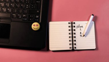 Dhaka, Bangladeş, 13 Mart 2020, pembe arka planda pürüzsüz bir emojisi olan bir dizüstü bilgisayarın yanında beyaz not defteri ve kalem. İş kavramı.
