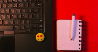 Dhaka, Bangladeş, 25 Mart 2020, pembe arka planda pürüzsüz bir emojisi olan bir dizüstü bilgisayarın yanında beyaz not defteri ve kalem. İş kavramı.