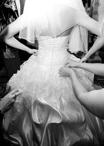 Bride and bridesmaids helps getting dress in her wedding dress