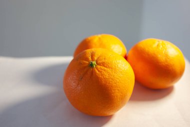 Beyaz masada üç taze mandalina var. Yaklaş.