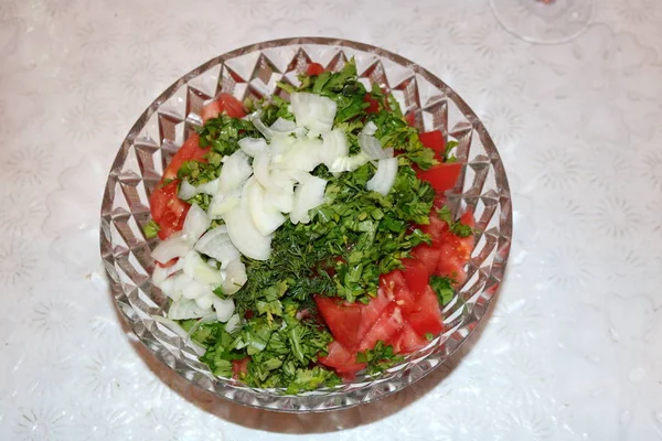 In a crystal Soviet salad bowl, a chopped salad of fresh vegetables onion, parsley, dill, cilantro, tomatoes without dressing stands on a white Soviet tablecloth. Vegetable salads contain a huge amount of minerals and vitamins useful for the body.
