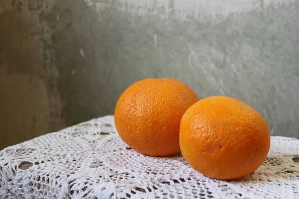 Orange two oranges on a white table cloth hand-knitted by a concrete gray wall in divorces in the loft. Distant orange in focus. It is a symbol of marriage, love, fertility, prosperity, tranquility. Widely used in medicine, dietetics, cosmetology.