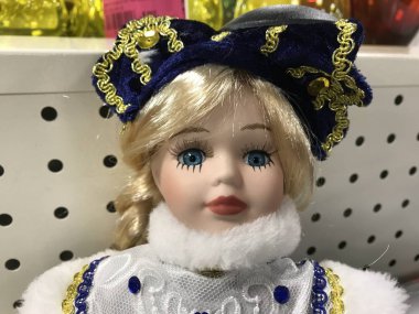 Dehşete kapılmış kar kızı oyuncağı. Mavi gözlü sarışın bir bebeğin portresi. Tezgahta beyaz elbiseli mavi bir fiyonk. 