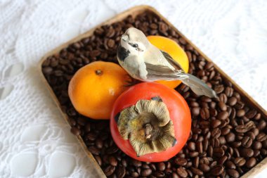 Yapay bir kuş, beyaz örülmüş bir masa örtüsüne karşı bir tepsi kahve çekirdeğinin üzerine oturmuş.. 