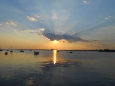 Güneş, balıkçı teknelerini aydınlatan bir bulutun içinden sakin bir denizde batar. Karadeniz, Pomorie, Bulgaristan, 2014. Fotoğraf: Nikon, Coolpix S3100.