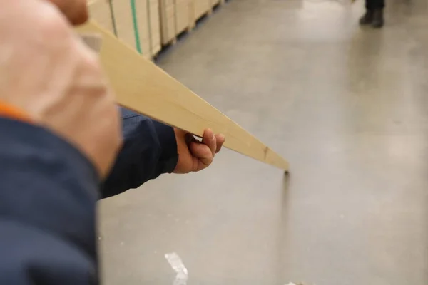 A view of a man\'s hand holding a long planed stick in the middle checking its evenness in the store. Shot under shop lighting. It can serve as a background for further work or an independent illustration.