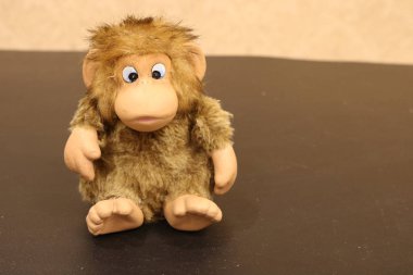 Oyuncak bir maymun bej bir duvara karşı soldaki siyah bir masada oturuyor. Fotoğraf ileri çalışma ya da kendini tanıtma için uygundur..