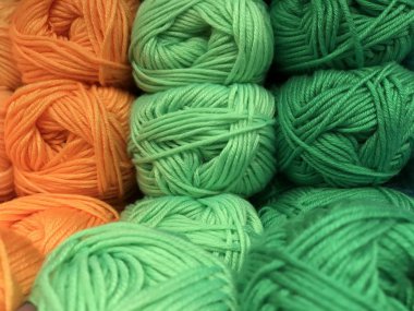 Texture of different sharpness from tangles of yarn in orange and green shades laid out in vertical rows. Mobile photo with store lighting.